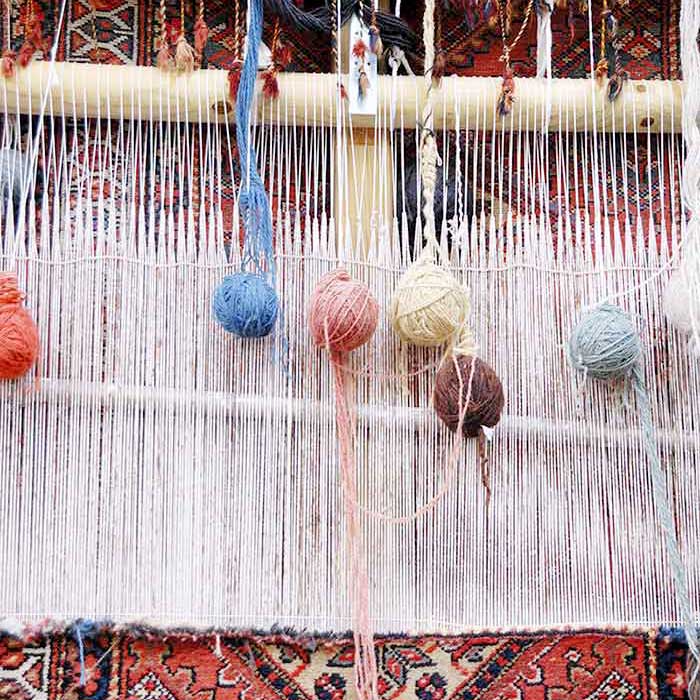 riparazione-tappeti-melzo-4 Gomitoli di filato colorato appesi al telaio con motivi intrecciati sullo sfondo, ideali per la riparazione tappeti o il restauro tappeti a Melzo.
